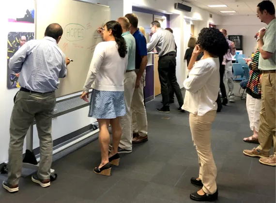 Crowd of people looking at a man write on a whiteboard